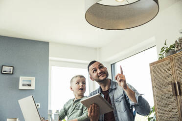 Man sitting with son pointing at pendant light in smart home - UUF23397