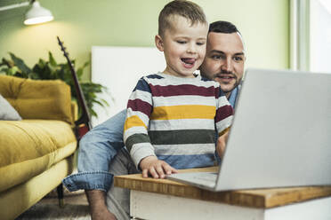 Man with son watching video on laptop in living room at home - UUF23403