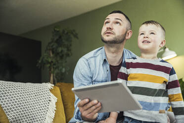 Father and son in living room looking away - UUF23413