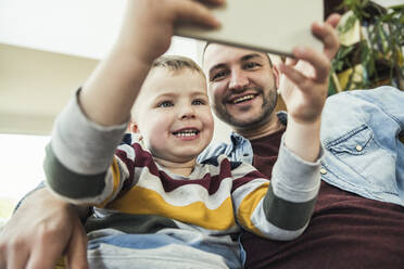 Lächelnder Vater sieht seinen Sohn an, der zu Hause sein Smartphone benutzt - UUF23417