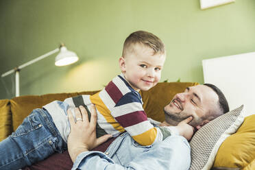 Niedlicher Junge liegt mit seinem Vater auf dem Sofa im Wohnzimmer zu Hause - UUF23427