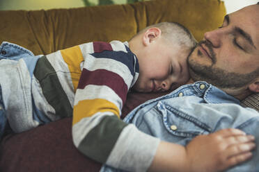 Father and son sleeping on sofa in living room at home - UUF23431