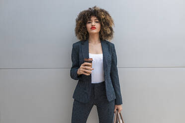 Businesswoman with purse having coffee in front of gray wall - JRVF00643