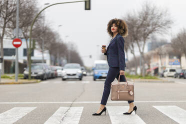 Gut gekleidete Geschäftsfrau mit Handtasche beim Überqueren der Straße in der Stadt - JRVF00645