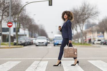 Well-dressed businesswoman with purse crossing road in city - JRVF00645