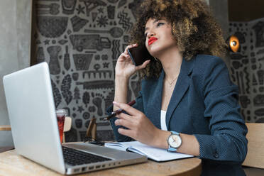 Female freelance worker talking on mobile phone at coffee shop - JRVF00655