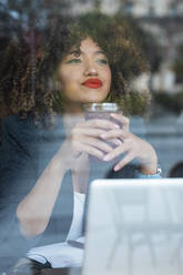 Beautiful businesswoman day dreaming while holding iced coffee in front of laptop at cafe - JRVF00657