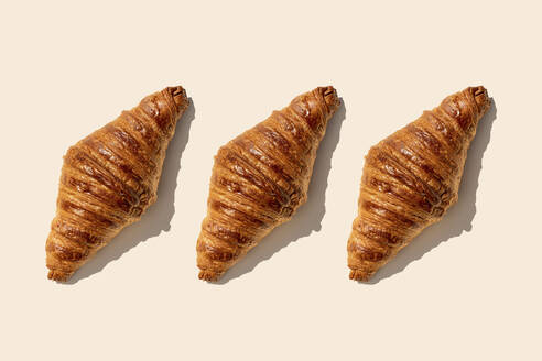 Butter croissants in a row on beige background - GEMF04801