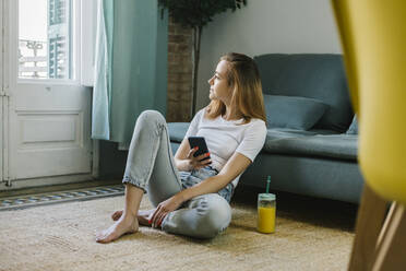 Junge Frau schaut weg, während sie zu Hause auf dem Teppich sitzt - XLGF01839