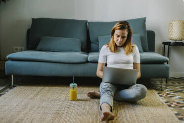 Rothaarige Frau benutzt Laptop, während sie zu Hause auf dem Teppich sitzt - XLGF01842