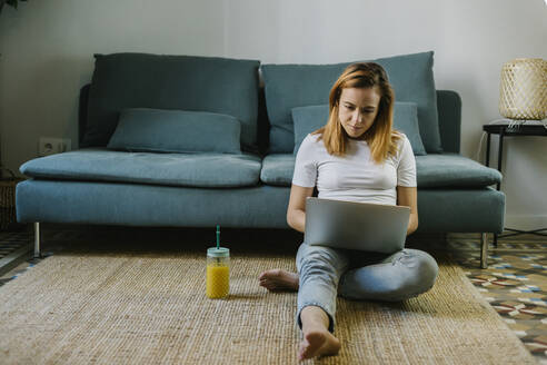 Rothaarige Frau benutzt Laptop, während sie zu Hause auf dem Teppich sitzt - XLGF01842