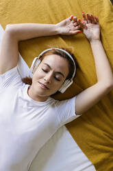 Young woman with eyes closed listening music while lying on bed at home - XLGF01858