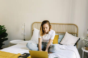 Junge Frau benutzt einen Laptop, während sie zu Hause auf dem Bett sitzt - XLGF01864