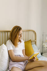 Rothaarige Frau liest Buch auf dem Bett zu Hause - XLGF01900