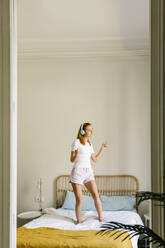 Glückliche Frau tanzt auf dem Bett zu Hause - XLGF01902