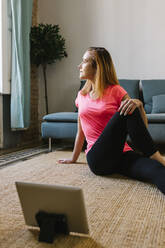 Redheaded woman using digital tablet while practicing exercise at home - XLGF01909