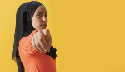 Arabische Frau mit Kopftuch, die auf einen gelben Hintergrund zeigt - JCCMF02572