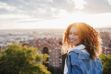 Junge Frau schaut bei Sonnenuntergang über die Schulter - EBBF03643