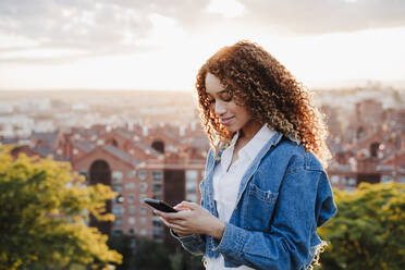 Junge Frau, die in der Stadt eine SMS auf einem Mobiltelefon schreibt - EBBF03645