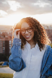 Junge Frau, die bei Sonnenuntergang eine Brille berührt - EBBF03649