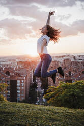 Fröhliche hispanische Frau springt bei Sonnenuntergang im Park - EBBF03659