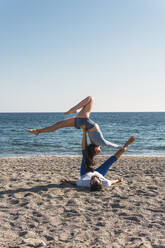 Couple doing acroyoga on the beach. Woman balancing on man - MGRF00222