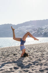 Mid erwachsene Frau übt Kopfstand am Strand während sonnigen - MGRF00223