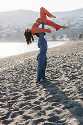 Mann trägt Frau bei Acroyoga-Übungen am Strand - MGRF00227