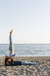 Couple kissing while practicing acroyoga on beach during sunny day - MGRF00231