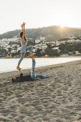 Woman balancing on man while exercising at beach - MGRF00232