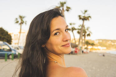 Beautiful woman looking over shoulder at beach - MGRF00233