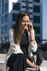 Geschäftsfrau, die an einem sonnigen Tag mit einem Mobiltelefon telefoniert und ein digitales Tablet benutzt - JRVF00663