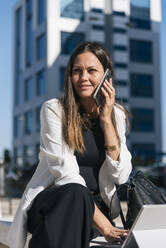Geschäftsfrau schaut weg, während sie mit einem Mobiltelefon spricht - JRVF00664