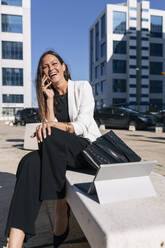 Fröhliche reife Geschäftsfrau, die auf einer Bank sitzend mit ihrem Smartphone telefoniert - JRVF00665