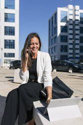 Eine Unternehmerin benutzt ein digitales Tablet, während sie an einem sonnigen Tag mit ihrem Handy telefoniert - JRVF00666