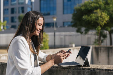Ältere Geschäftsfrau mit digitalem Tablet und Smartphone an einem sonnigen Tag - JRVF00678