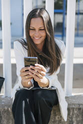 Businesswoman using smart phone in front of fence - JRVF00691