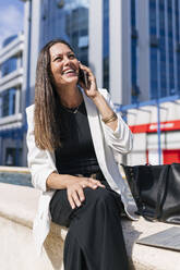 Weibliche Unternehmerin, die an einem sonnigen Tag im Sitzen mit einem Mobiltelefon spricht - JRVF00698