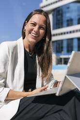 Smiling businesswoman with digital tablet sitting on sunny day - JRVF00704