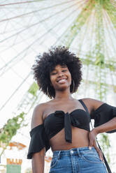 Smiling woman with hand on hip standing in amusement park - JRVF00731