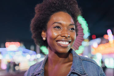 Lächelnde nachdenkliche Frau im beleuchteten Vergnügungspark - JRVF00752