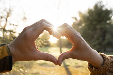 Man and woman's hands making heart shape symbol during sunset - JCCMF02604