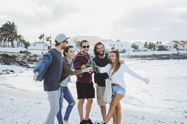 Glückliche Freunde stoßen mit Bierflaschen an, während sie am Strand stehen - DGOF02190