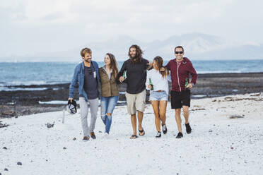 Smiling friends with arm around walking together on sand - DGOF02193