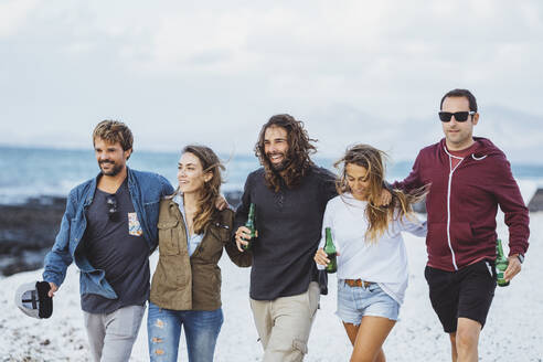 Männer und Frauen mit Bierflaschen gehen zusammen am Strand spazieren - DGOF02194