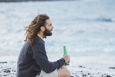 Nachdenklicher junger Mann mit Bierflasche am Strand - DGOF02195