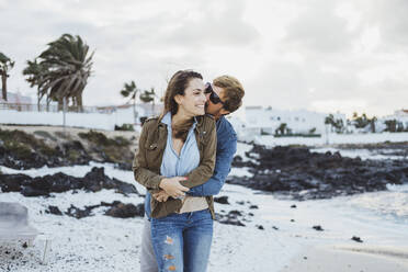 Mid adult boyfriend kissing while embracing girlfriend at beach - DGOF02199