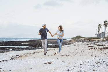 Carefree couple holding hands while running on beach - DGOF02209