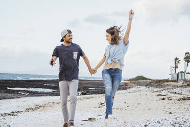 Glückliche Freundin hält die Hand ihres Freundes beim Laufen am Strand - DGOF02210