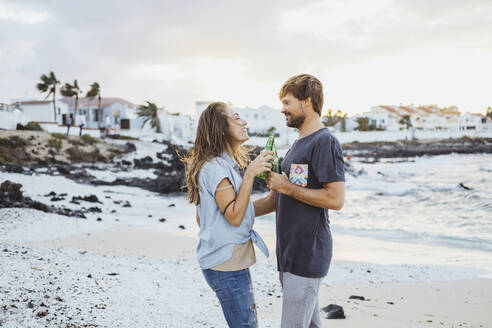 Couple toasting beer bottles while standing at beach - DGOF02213